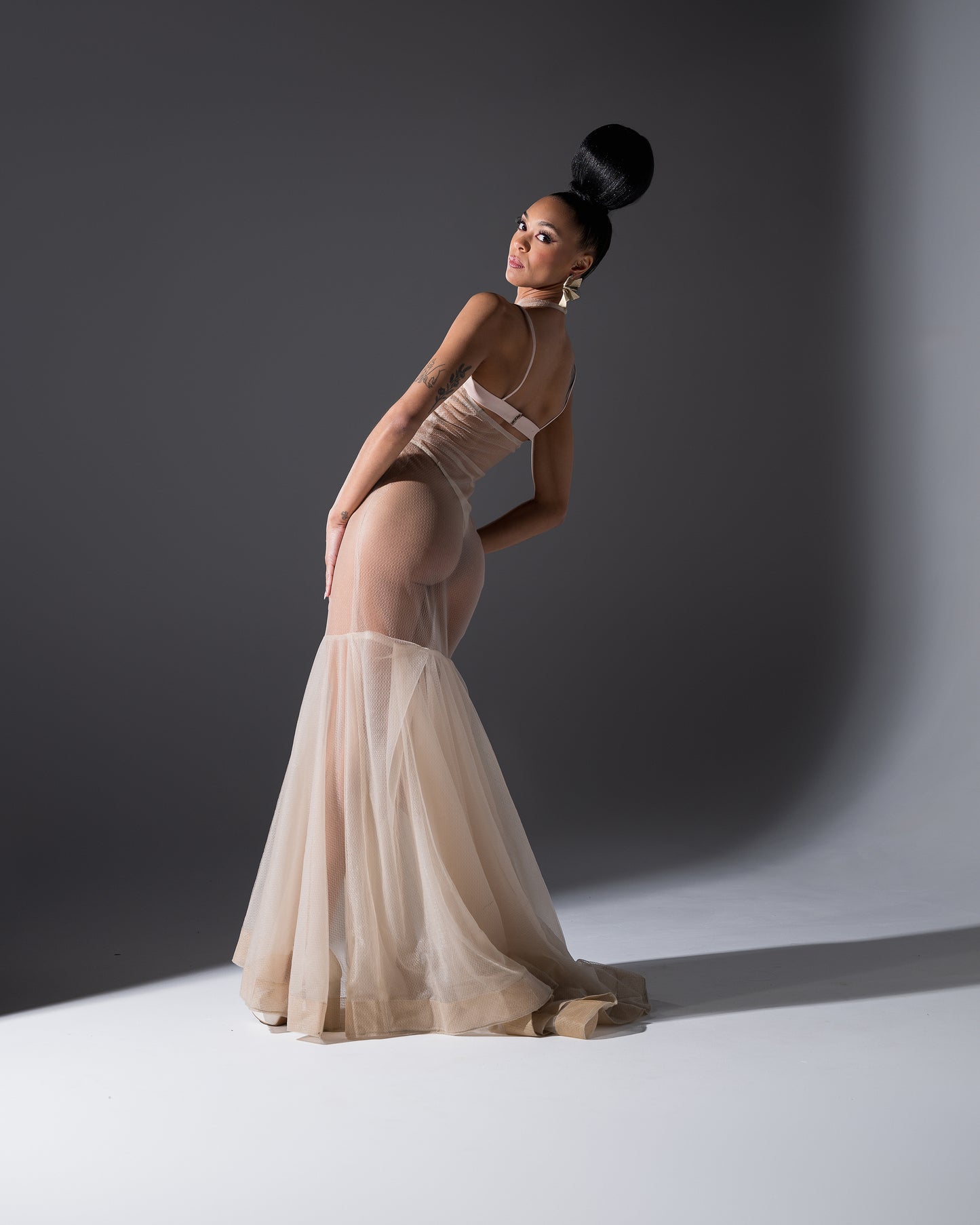 Woman in a sheer beige dress posing against a dark background