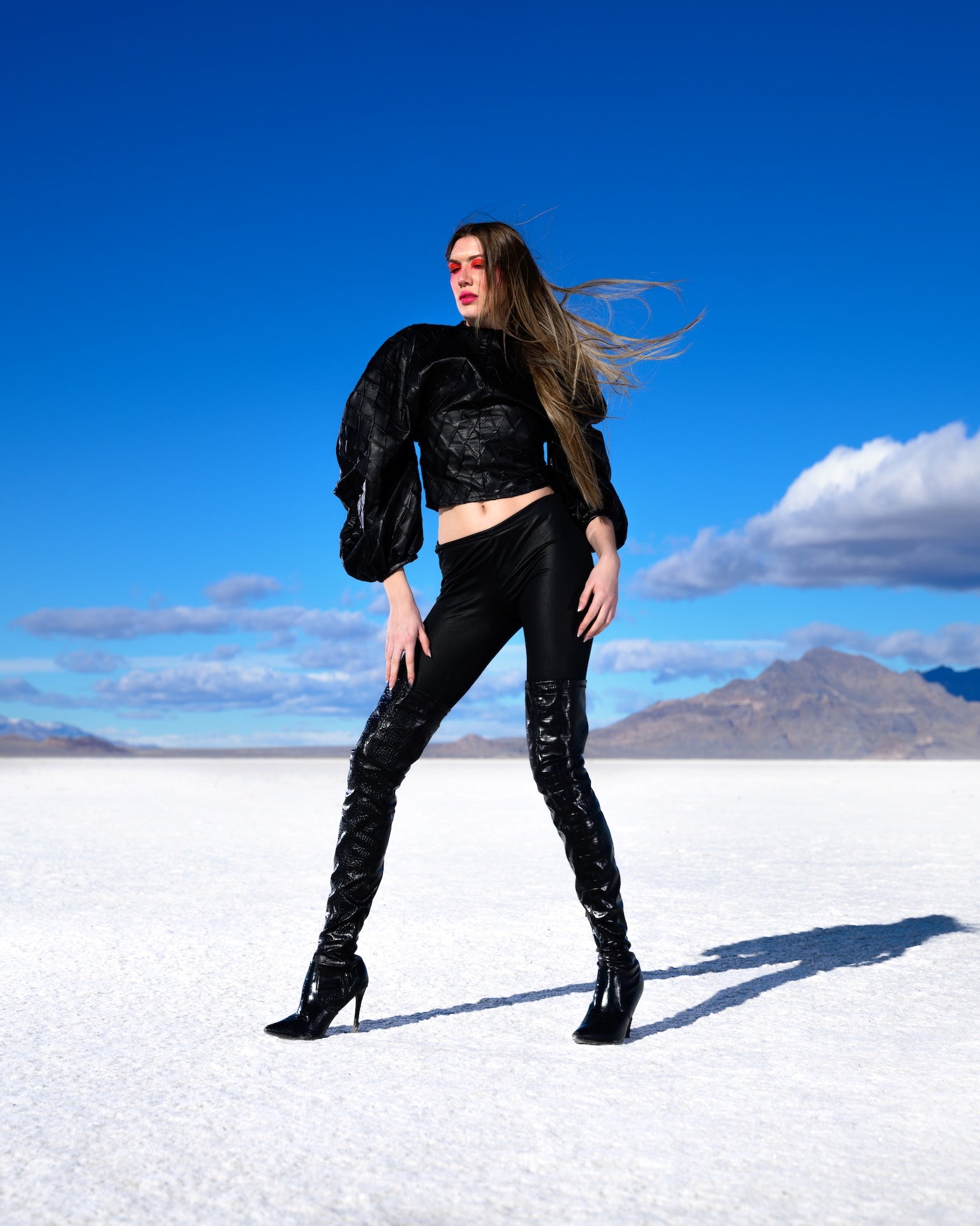 Woman in black outfit standing on a salt flat with mountains and blue sky in the background