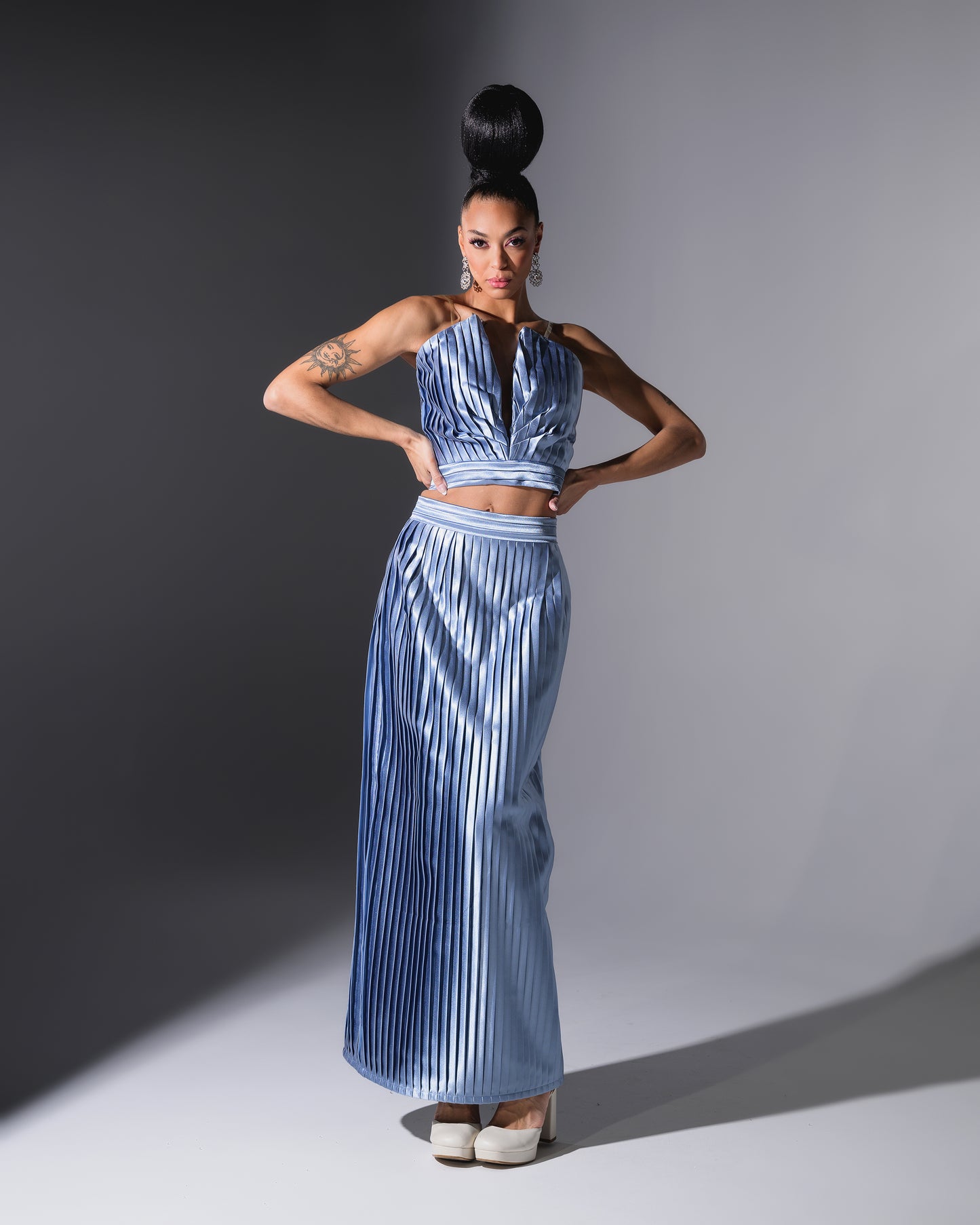 Woman wearing a blue metallic outfit posing against a gray background