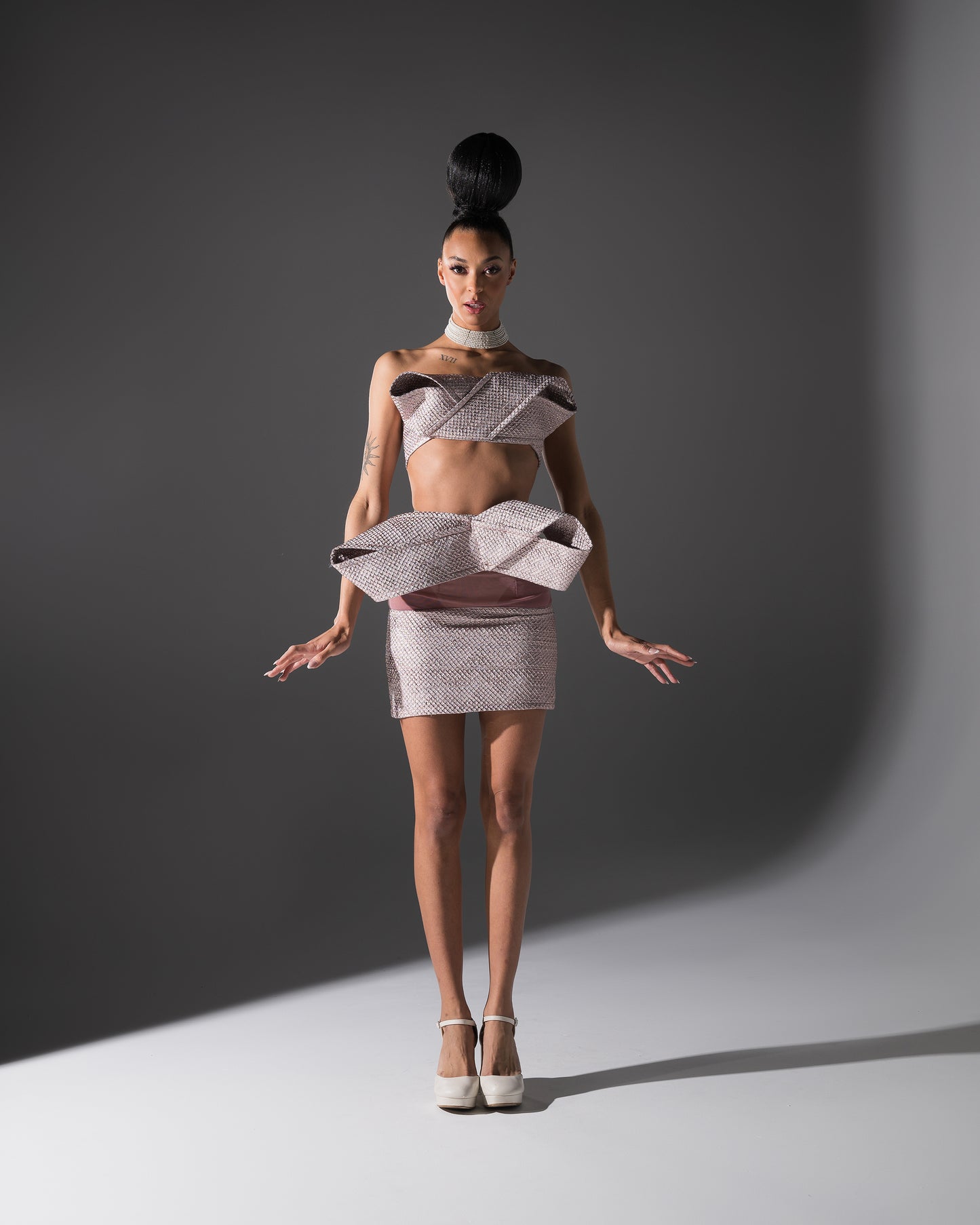 Model wearing a futuristic outfit with ruffled top and skirt against a gray background