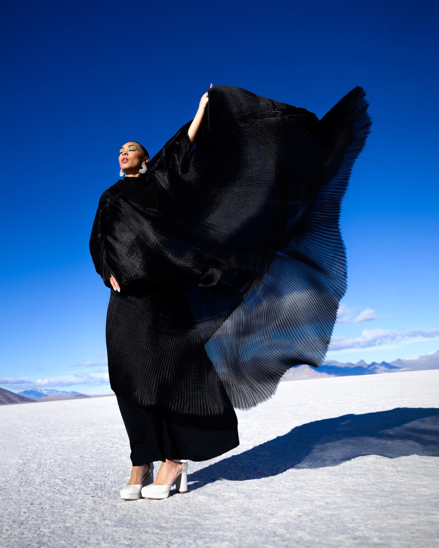 Person wearing a flowing black dress against a blue sky and white landscape