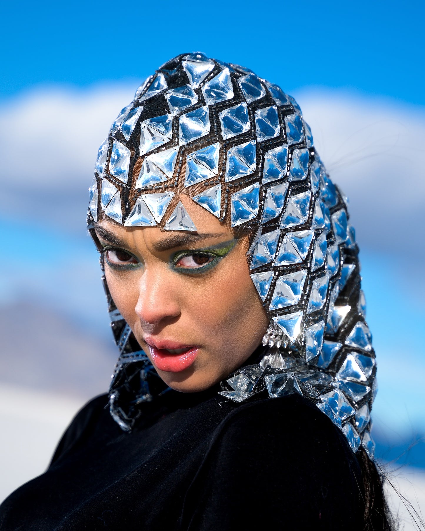 Person wearing a futuristic, geometric-patterned headpiece against a blue sky.