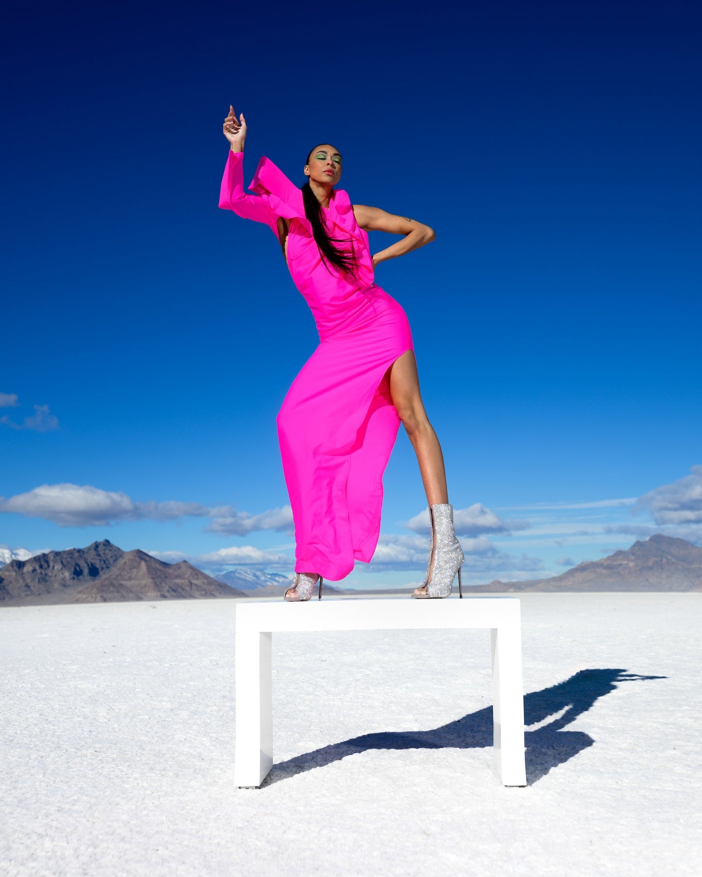 Person in a bright pink dress posing on a salt flat with mountains in the background