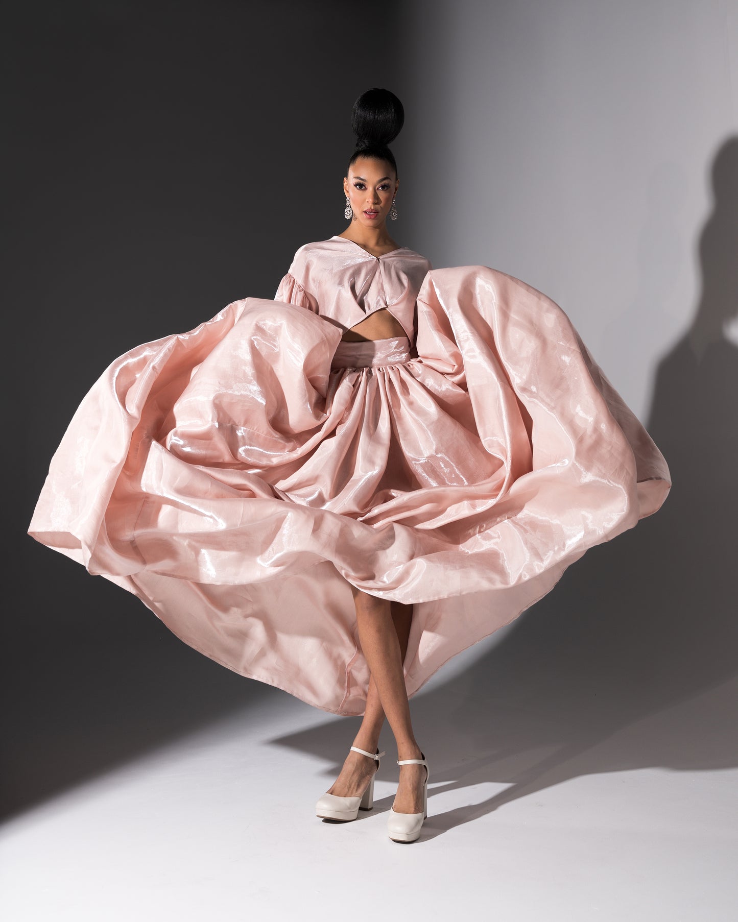 Model wearing a pink, voluminous dress against a gray background