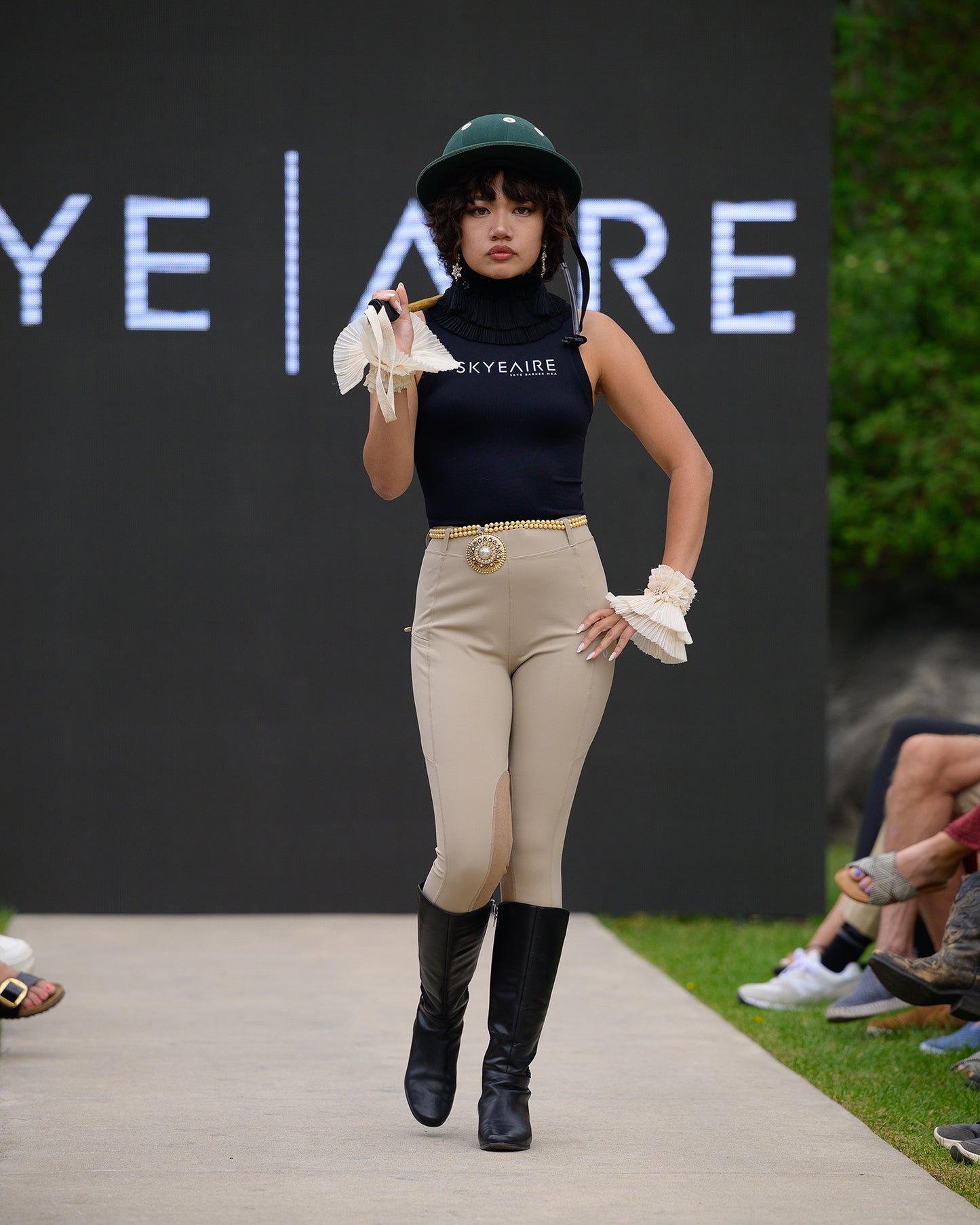 Model on a fashion runway wearing equestrian attire with 'Skyeaire' branding in the background.