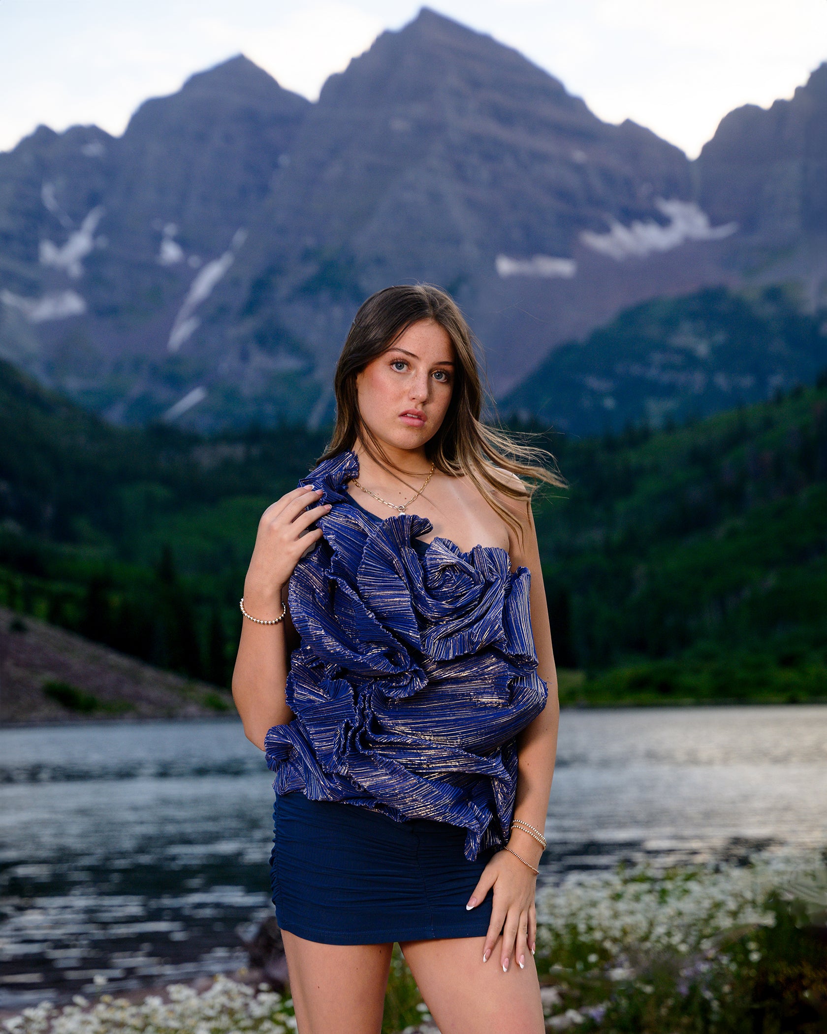Woman in a blue strapless top and shorts standing in front of mountains and a lake.